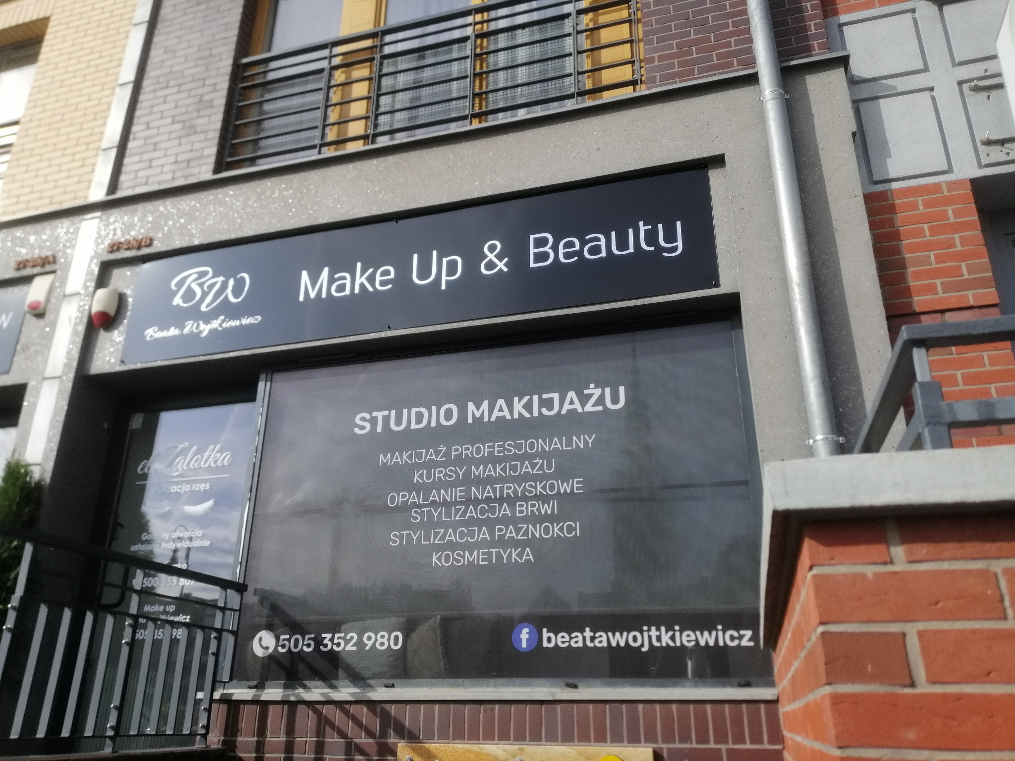 Fasada budynku z szyldem 'BW Make Up & Beauty' oferującego profesjonalny makijaż, kursy makijażu, opalanie natryskowe, stylizację brwi, paznokci i kosmetykę. Widoczne numery telefonów i adres...