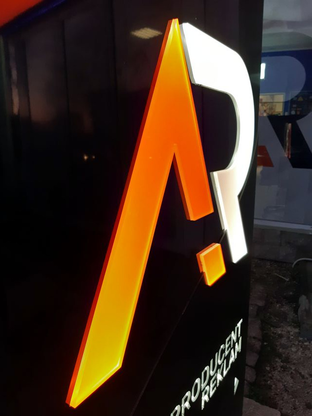 Podświetlany szyld z logo firmy, litera A w kolorze pomarańczowym przechodząca w żółty, obok litera R w kolorze białym, na czarnym tle