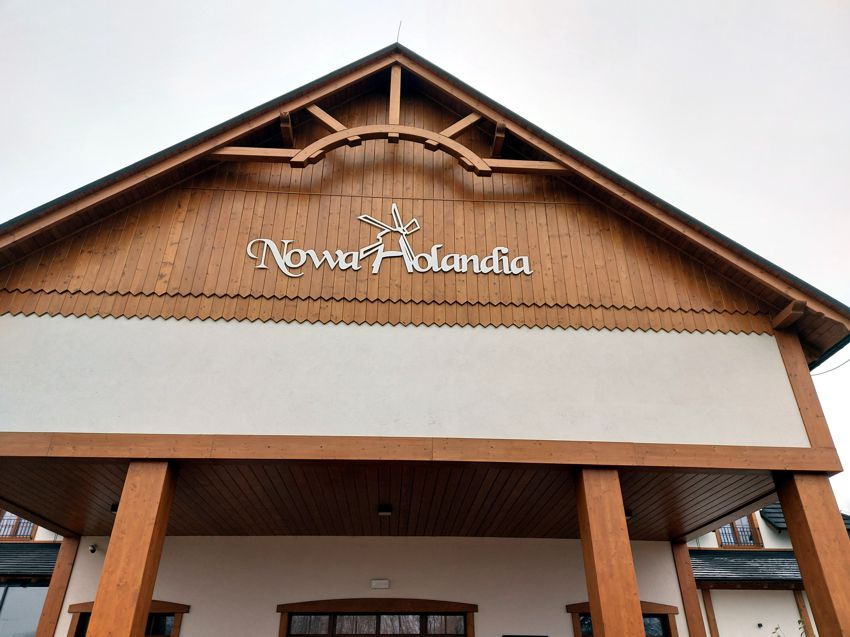 Fasada budynku z drewnianą konstrukcją i napisem 'Nowa Holandia' w górnej części.