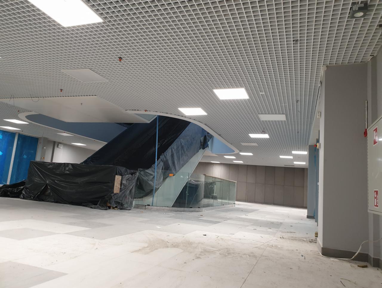 Montaż sufitu rastrowego w biurze, widoczne elementy konstrukcyjne, oświetlenie w suficie oraz zabezpieczone folią schody ruchome w tle.