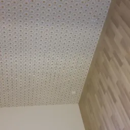 Ściana i sufit po remoncie: parkiet na ścianie, sufit pokryty tapetą w geometryczny wzór heksagonów w odcieniach beżu i szarości.