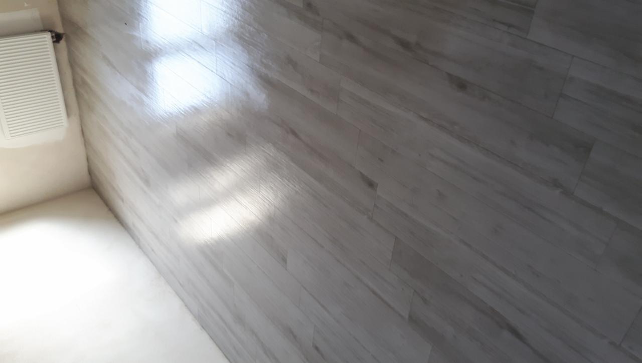 Wykończona łazienka z panelami ściennymi imitującymi drewno, grzejnik na ścianie, widoczne odbicie światła na powierzchni paneli.