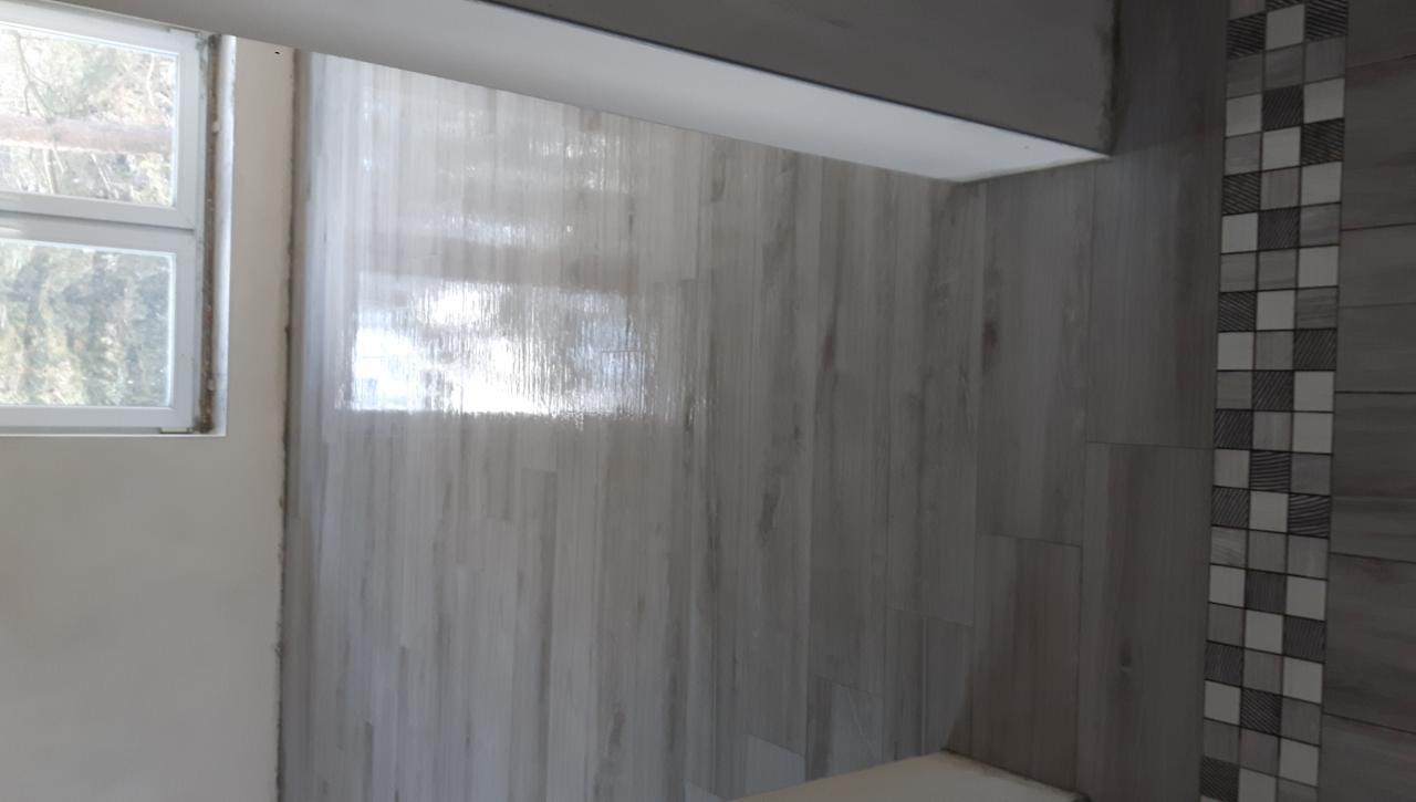 Świeżo położone, błyszczące płytki imitujące drewno na ścianie łazienki, z dekoracyjnym pasem mozaiki w szaro-białą szachownicę po prawej stronie i oknem po lewej, widoczne ślady fugowania.