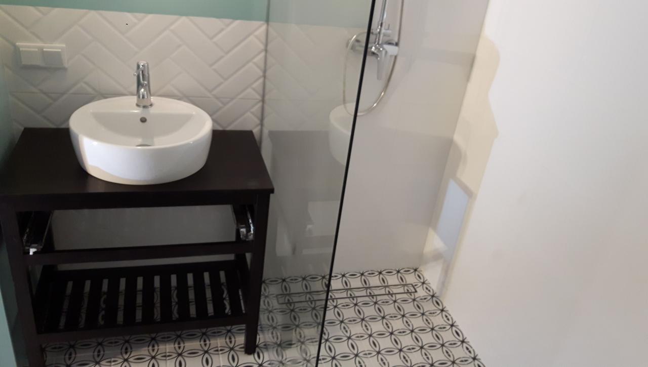 Nowoczesna łazienka z okrągłą umywalką nablatową na ciemnym drewnianym regale, białe płytki ułożone w jodełkę na ścianie i wzorzysta posadzka, kabina prysznicowa ze szklaną ścianką.