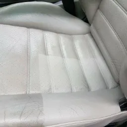 Jasnoszare skórzane siedzenie samochodowe, połowa wyczyszczona, ukazująca różnicę przed i po zabiegu, widoczne perforacje i szwy.