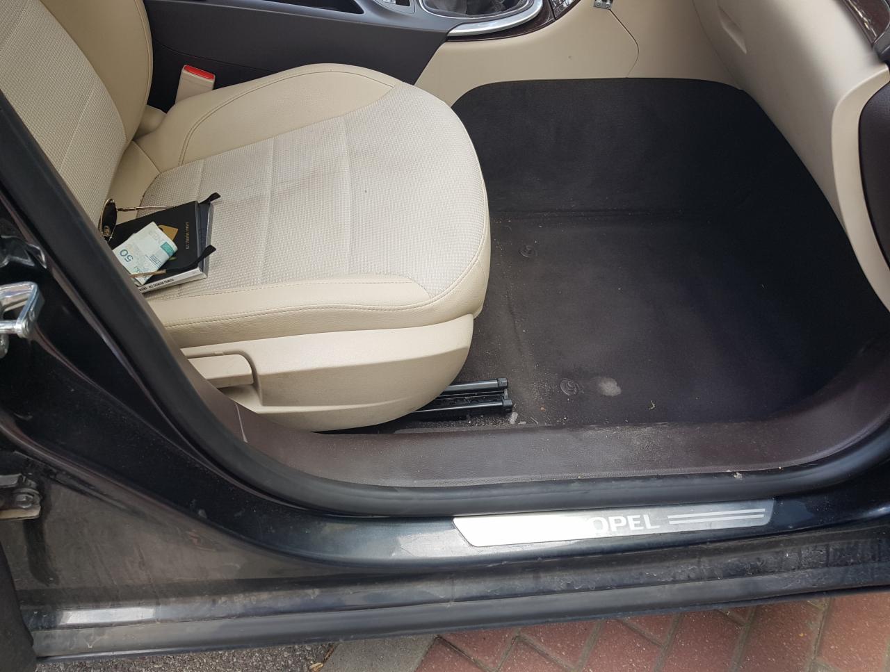 Wnętrze samochodu Opel z beżową tapicerką i czarnym dywanikiem podłogowym, na siedzeniu leżą okulary, portfel i banknot 50 euro.