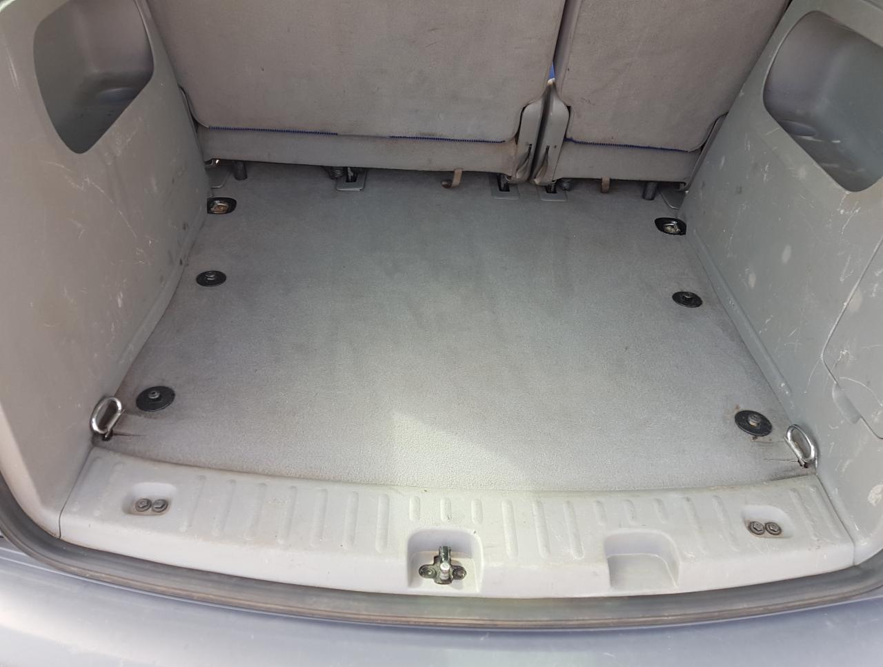 Wnętrze bagażnika samochodu z szarą wykładziną, widoczne uchwyty mocujące i elementy tapicerki.