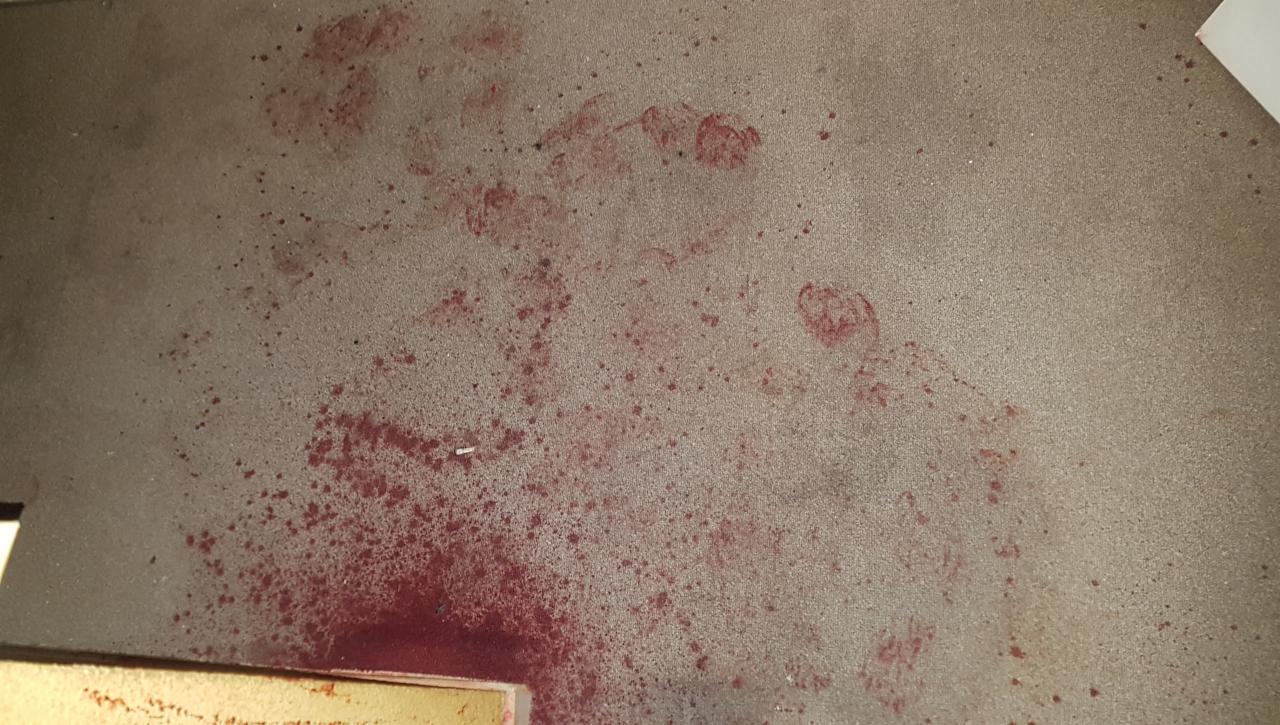 Brudny, beżowy dywan z plamami i odciskami stóp w kolorze czerwonym.