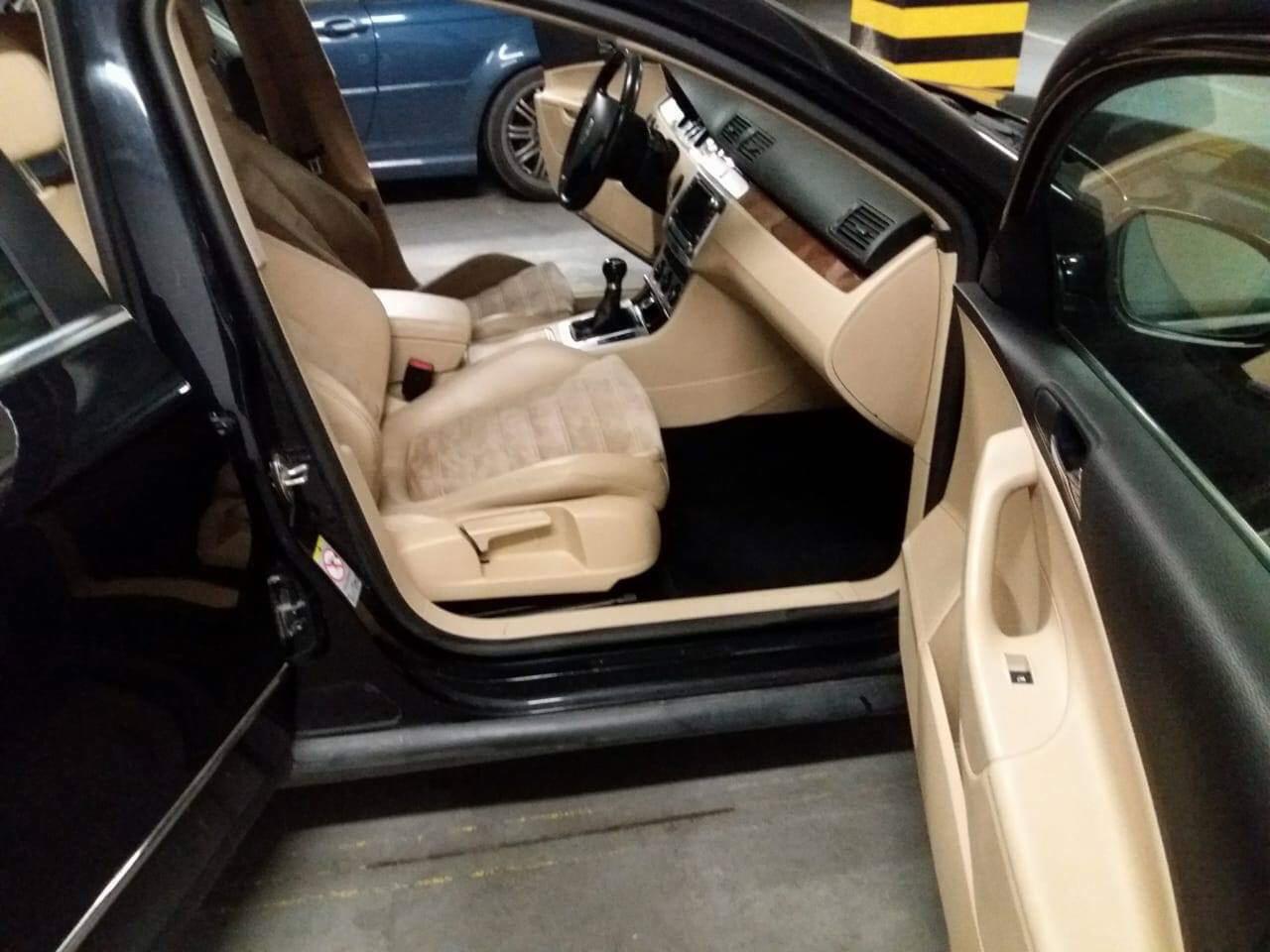 Wnętrze samochodu z beżową tapicerką, widoczne fotele z wzorem, czarne dywaniki i otwarte drzwi, zaparkowany na parkingu podziemnym.