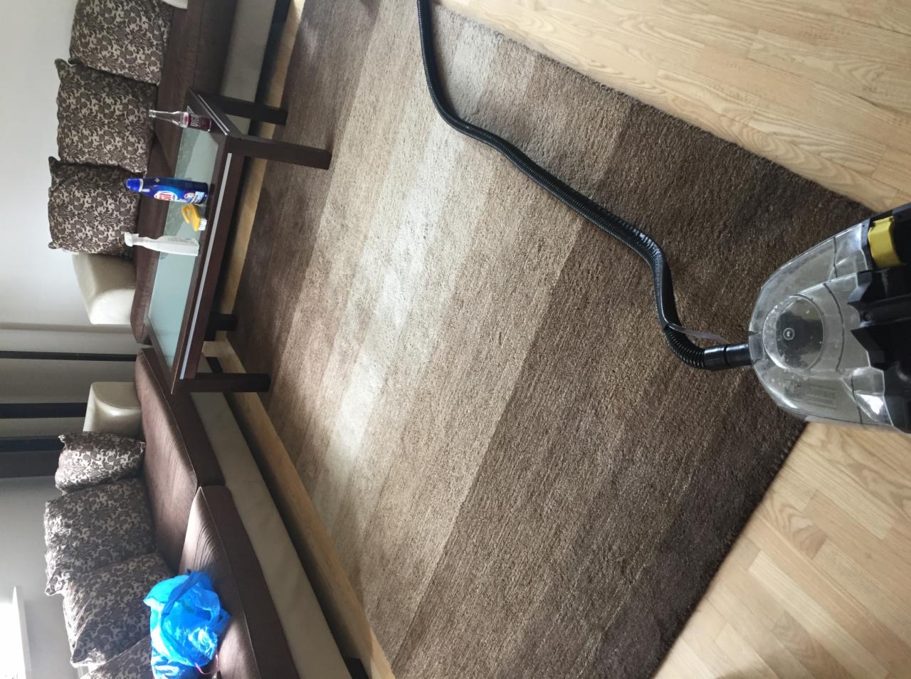 Czyszczenie brązowego dywanu z geometrycznym wzorem za pomocą odkurzacza piorącego; widoczne ślady czyszczenia.