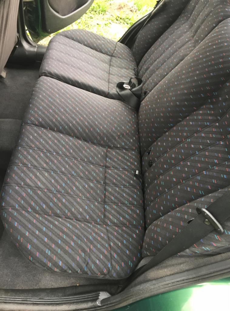 Wnętrze samochodu: tylna kanapa z tapicerką w czarno-szare paski z akcentami czerwieni i błękitu, widoczny pas bezpieczeństwa.