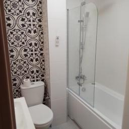 Fryderyk Trojanowski - Kompaktowa łazienka z białą armaturą, kabiną prysznicową nad wanną oraz ścianą akcentującą z czarno-białymi płytkami w stylu retro, papier toaletowy na spłuczce.