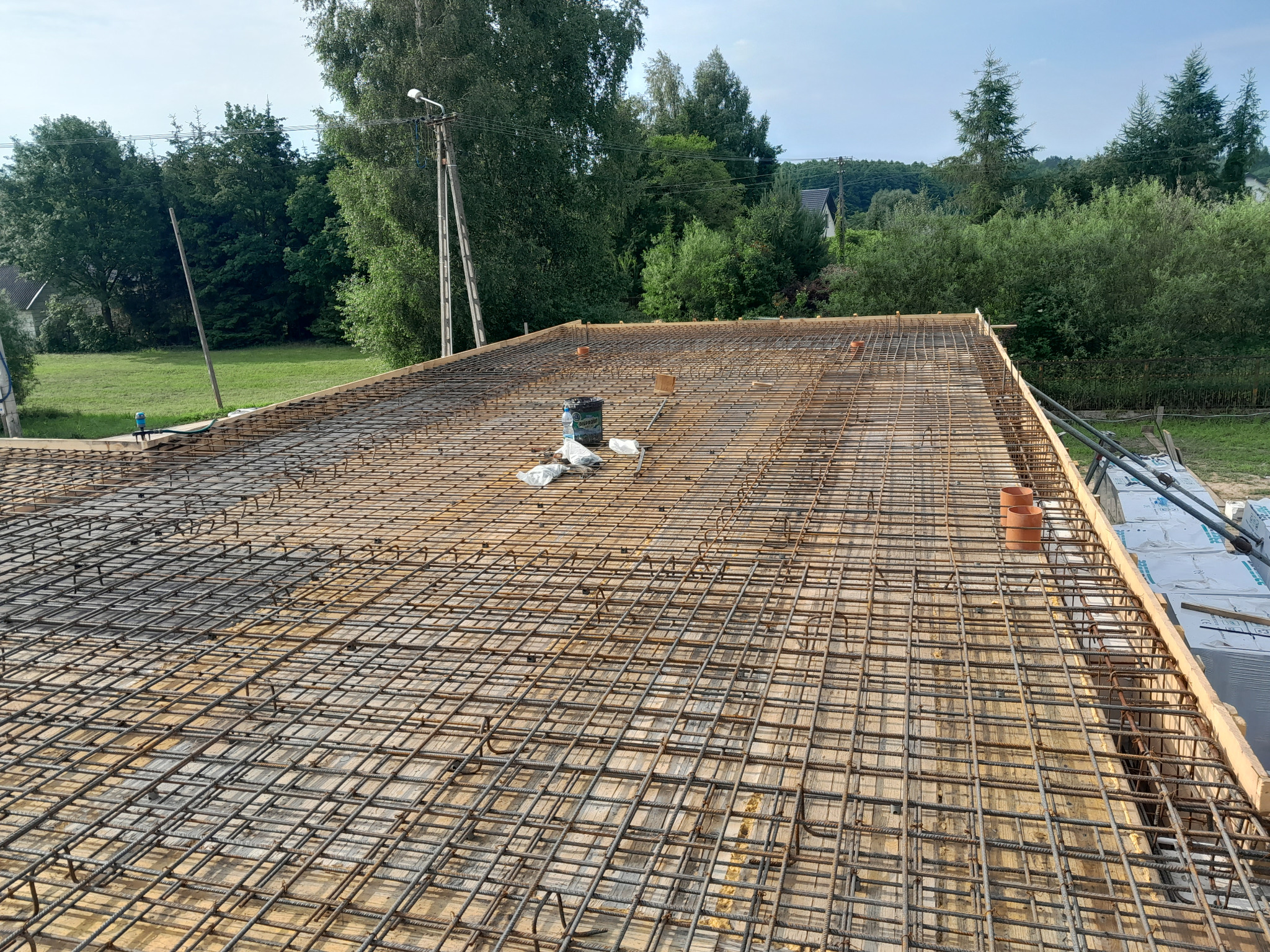 Zbrojenie płyty fundamentowej z widocznymi elementami szalunku i otoczeniem zieleni