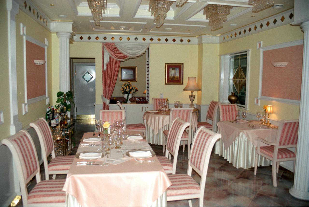 Elegancka sala bankietowa w odcieniach beżu i różu z kolumnami, kryształowymi żyrandolami, stołami nakrytymi różowymi obrusami i krzesłami w biało-różowe paski, przygotowana do przyjęcia.