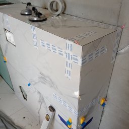 Jarosław Powroźnik - Wykończenie obudowy wanny płytkami marmuropodobnymi, zabezpieczonymi taśmą i przyssawkami. Widoczne poziomica i kliny do płytek. Prace glazurnicze w toku.