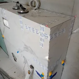 Wykończenie obudowy wanny płytkami marmuropodobnymi, zabezpieczonymi taśmą i przyssawkami. Widoczne poziomica i kliny do płytek. Prace glazurnicze w toku.