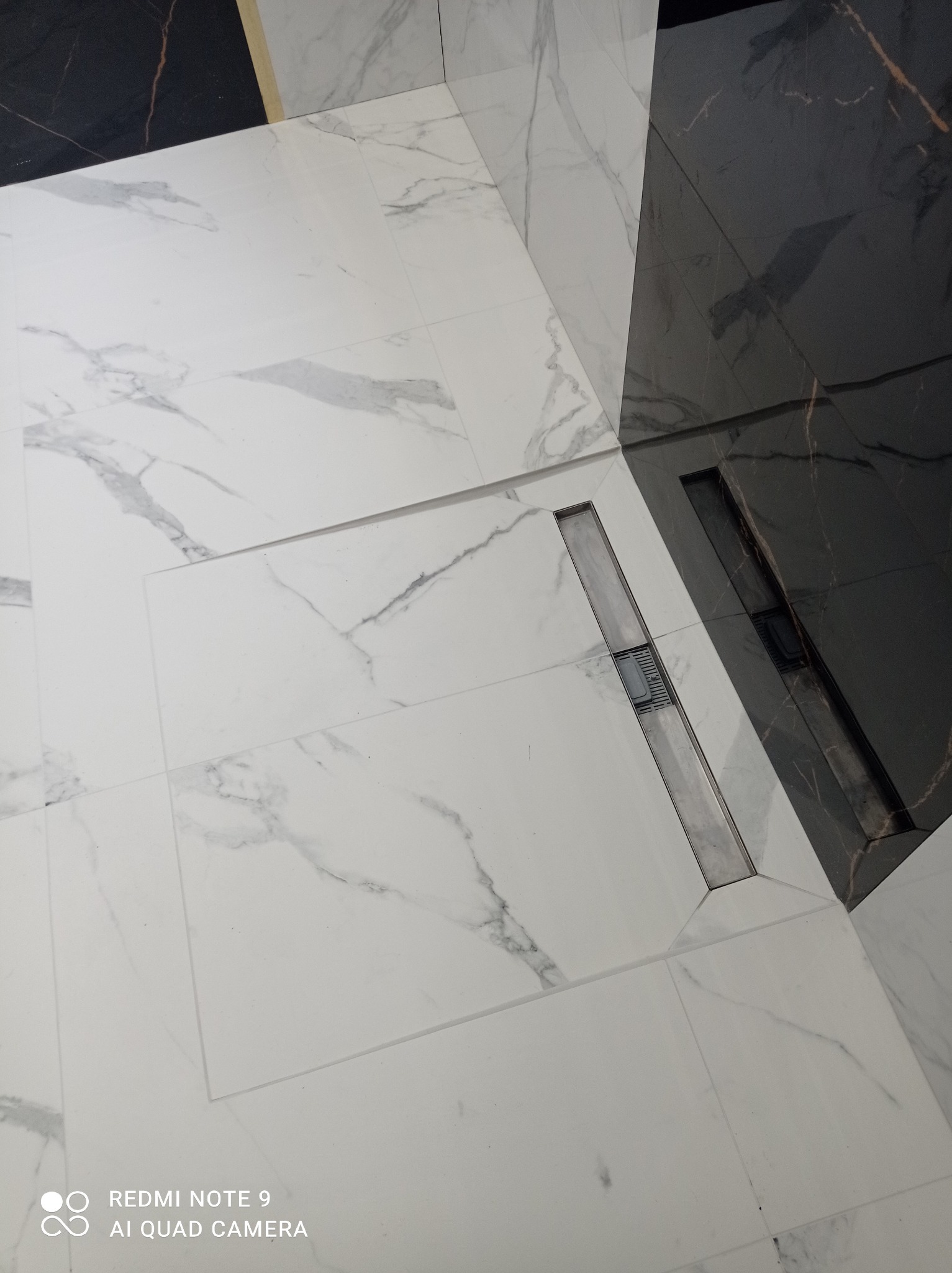 Białe i czarne płytki marmurowe z odpływem liniowym w kabinie prysznicowej. Nowoczesne wykończenie łazienki, elegancki design. Detal odpływu.