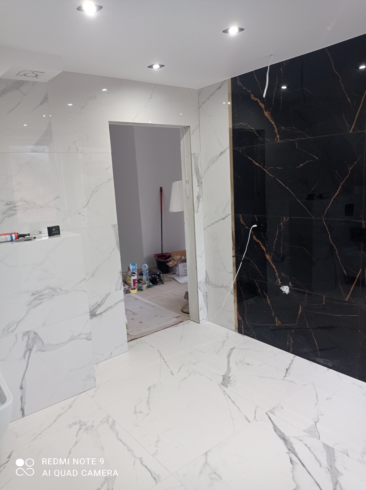Elegancka łazienka z czarno-białymi płytkami imitującymi marmur. Widoczne narzędzia i materiały budowlane, co sugeruje etap wykończenia.