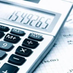 Kalkulator z wyświetloną kwotą 1549265 na tle kartki w kratkę z odręcznymi notatkami finansowymi.