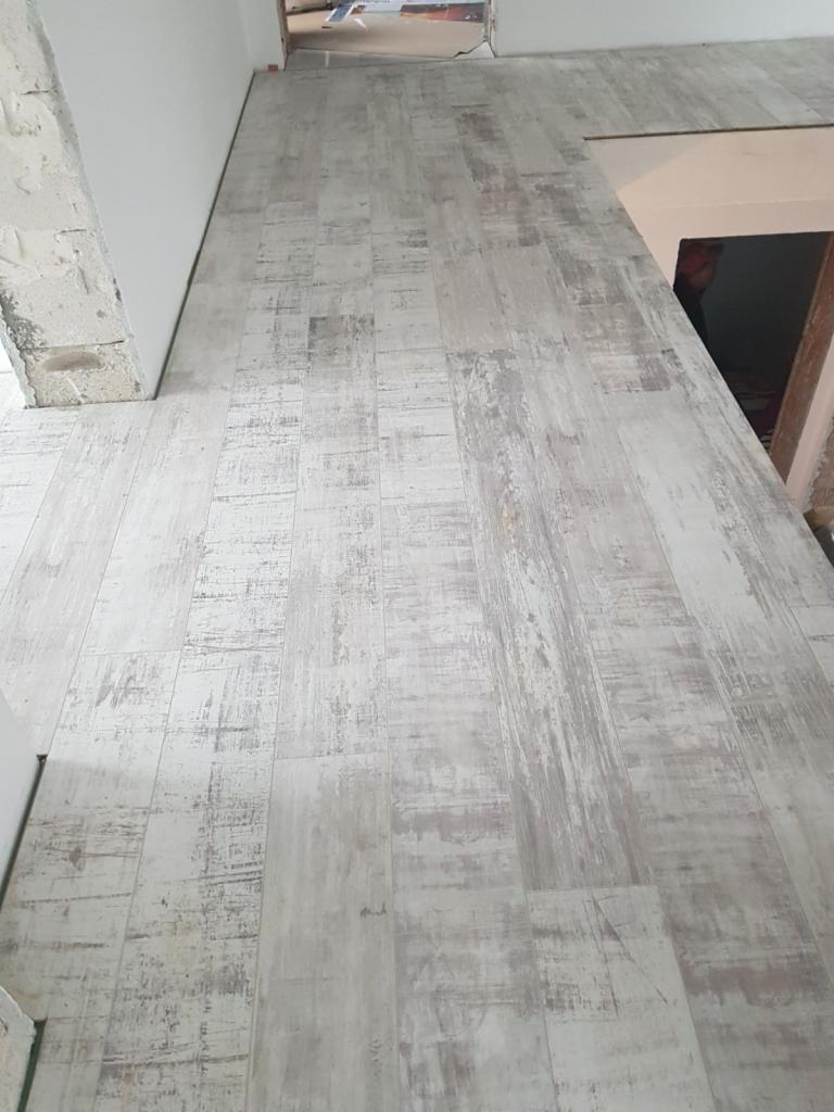 Ułożona podłoga z paneli o wzorze imitującym postarzane, bielone drewno w trakcie remontu. Widoczne surowe ściany i fragment schodów.