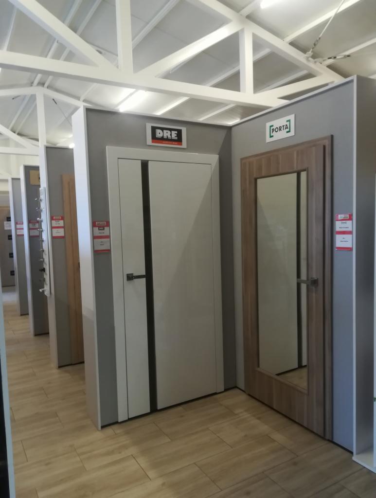 Ekspozycja modeli drzwi wewnętrznych DRE i Porta w salonie, widoczne różne style i wykończenia, podłoga z paneli imitujących drewno.