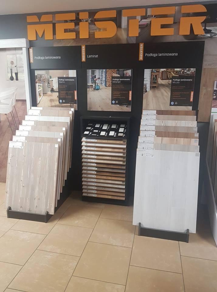 Ekspozycja paneli laminowanych marki Meister z różnymi wzorami i kolorami, prezentowana w sklepie na stojakach i półkach.