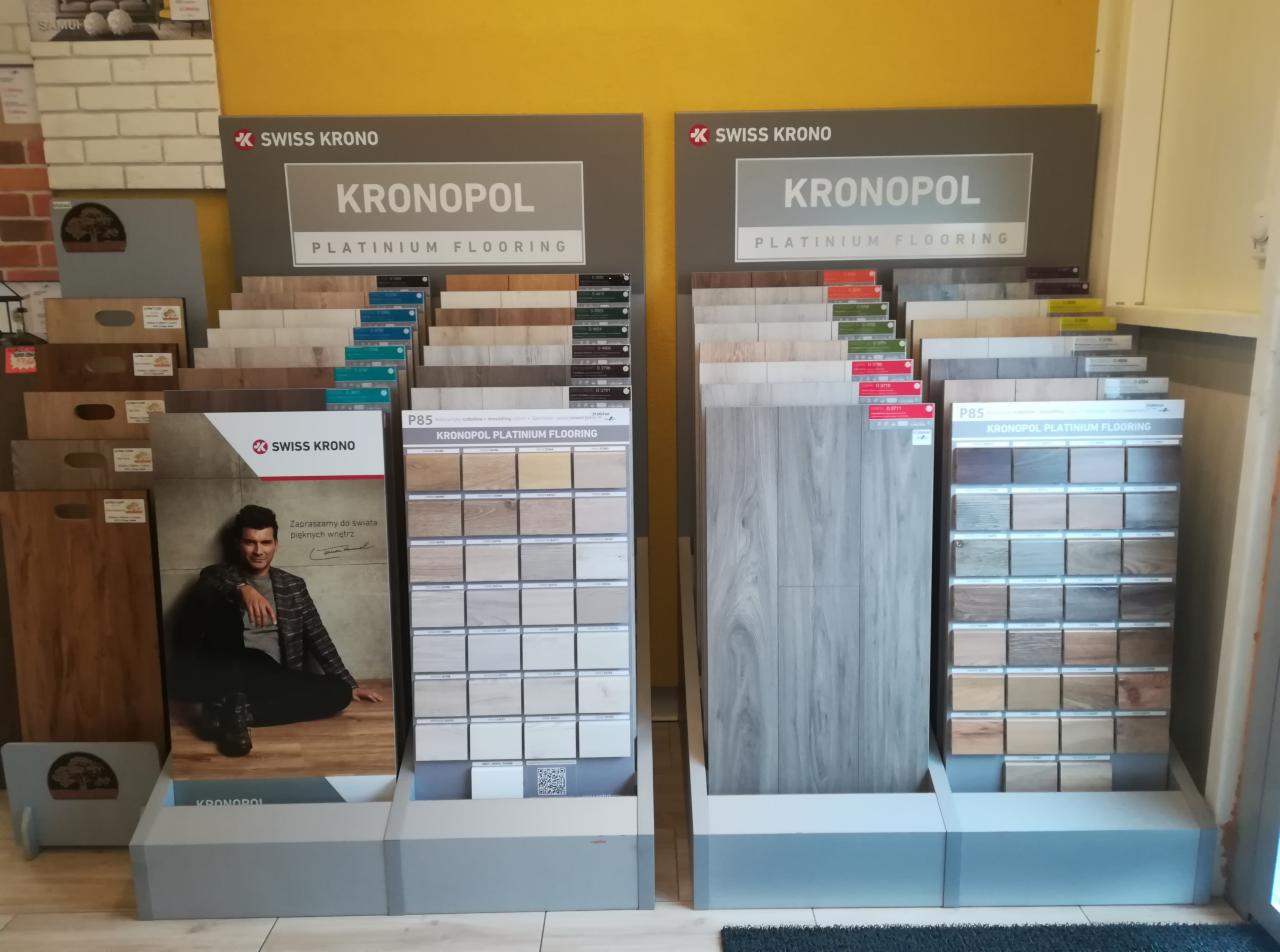 Ekspozycja wzorników paneli podłogowych marki Kronopol w sklepie, widoczne różne kolory i tekstury.