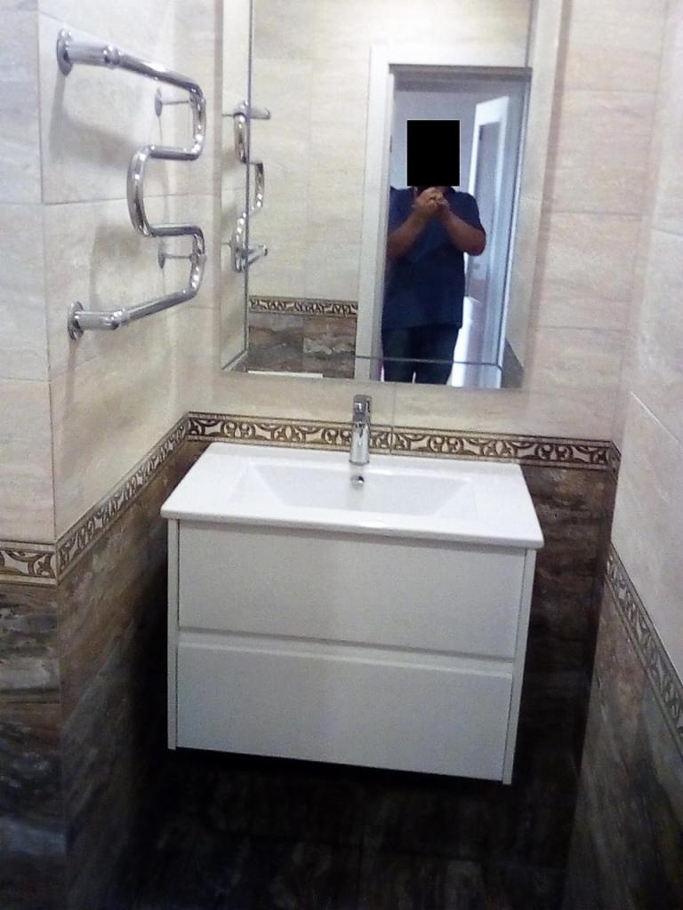 Łazienka po remoncie: biała szafka pod umywalką z dwoma szufladami, chromowana bateria, grzejnik drabinkowy na ścianie, lustro z odbiciem osoby robiącej zdjęcie.