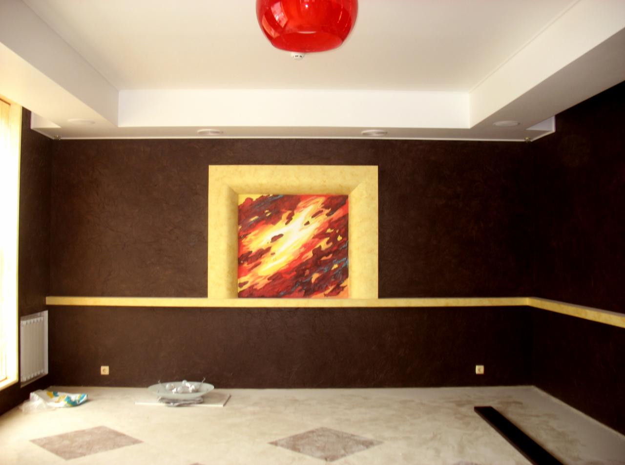Pokój z ciemnobrązowymi ścianami o teksturowanej powierzchni, żółtym pasem dekoracyjnym i wnęką z obrazem w podobnej kolorystyce, czerwona lampa sufitowa, częściowo zakryta podłoga w jasnych...
