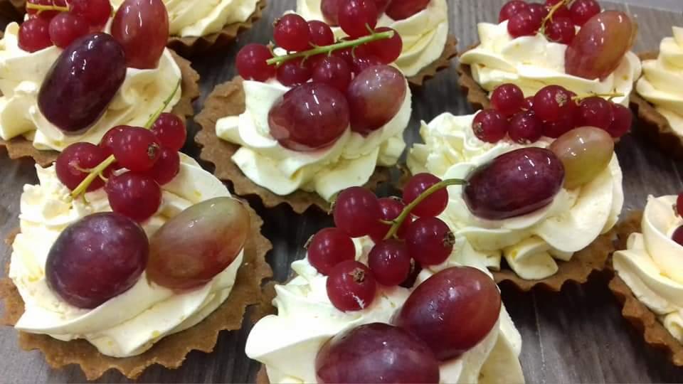 Kruche babeczki z kremem i owocami: ciemne winogrona, czerwone porzeczki, jasne winogrona. Widoczne detale kremu i faktura ciasta.