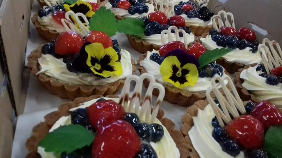 Tarty z kremem, świeżymi truskawkami, borówkami i jadalnymi bratkami w pudełku, ozdobione białymi czekoladowymi dekoracjami.