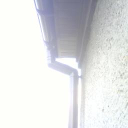 Osoba Prywatna.. - Szary system rynnowy zamontowany przy szorstkiej, jasnej ścianie budynku, widoczne elementy mocujące.