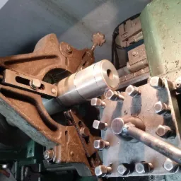 Obróbka metalowego wałka na tokarce; widoczne ślady chłodziwa i wióry metalu na maszynie.