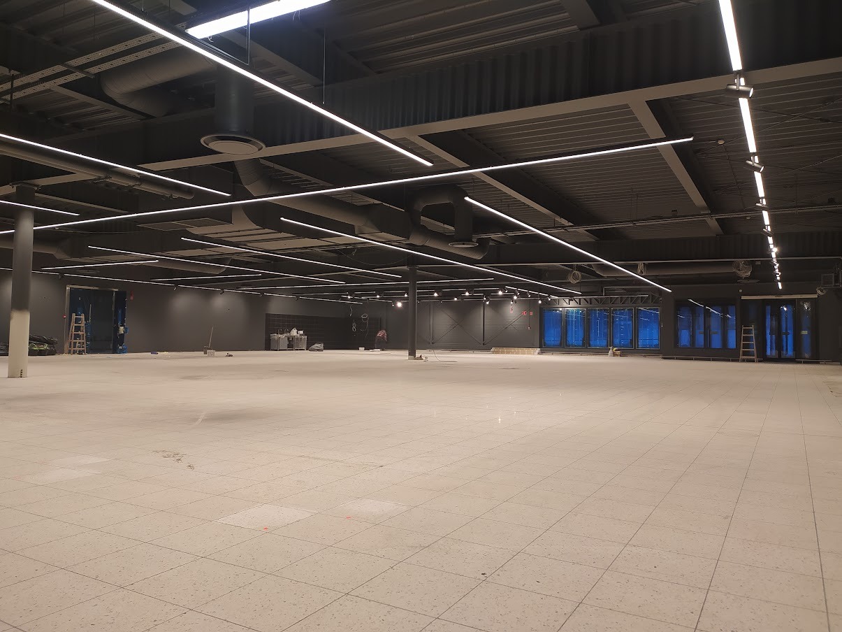 Wnętrze sklepu Netto w Żychlinie w trakcie prac wykończeniowych, widoczne zainstalowane, liniowe oświetlenie LED pod sufitem, szara kolorystyka ścian i sufitu, jasna podłoga z płytek, instalacje...