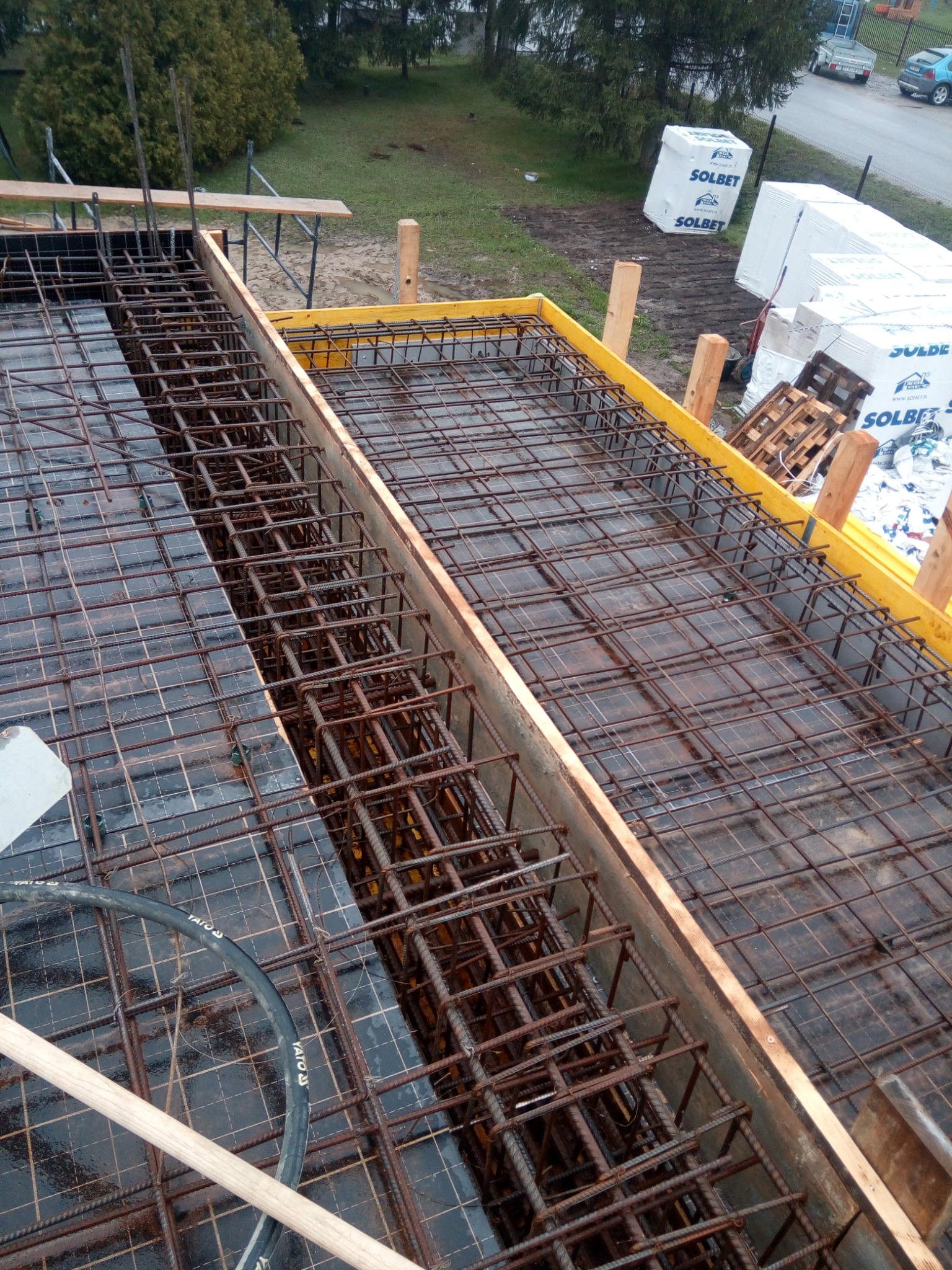 Zbrojenie fundamentów w szalunku z żółtymi elementami, widoczne bloczki Solbet w tle, oraz narzędzia YATO.