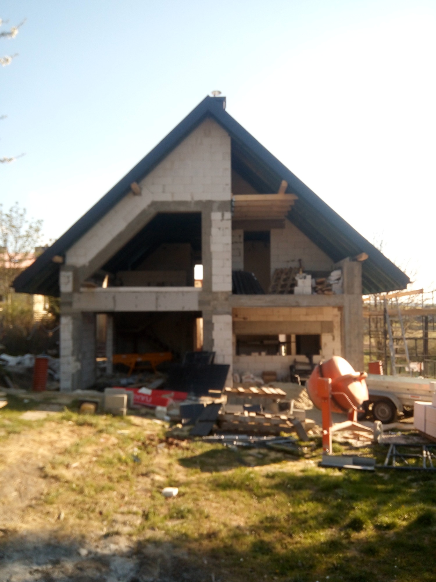 Surowy stan budowy domu murowanego w Rzeszowie z widoczną betoniarką i materiałami budowlanymi na zewnątrz, wczesny etap prac.