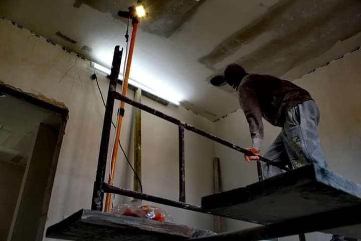 Pracownik na rusztowaniu, przygotowujący sufit do malowania, widoczne niedoskonałości i nierówności na powierzchni.