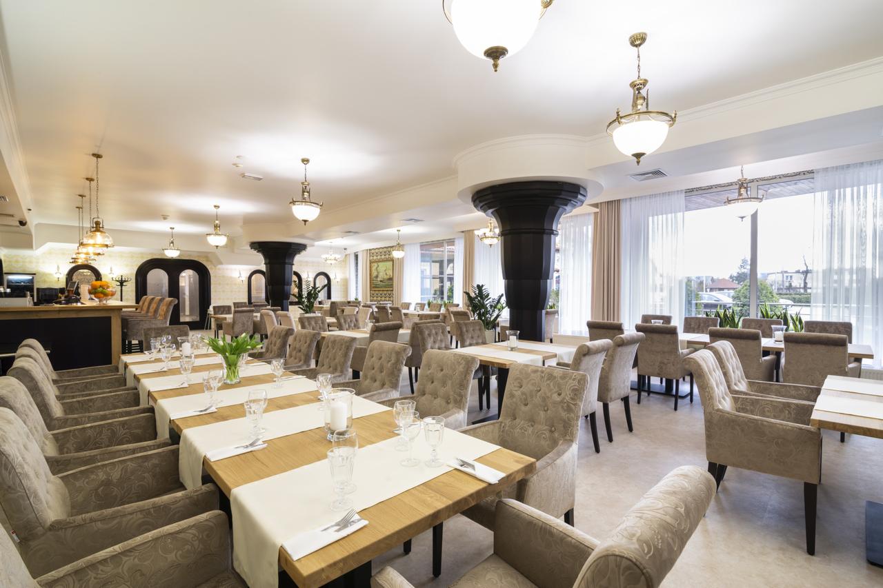 Elegancka sala restauracyjna z nakrytymi stołami, krzesłami w stylu Chesterfield i dekoracyjnymi kolumnami.