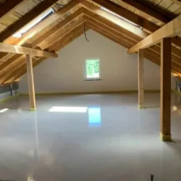 Poddasze z drewnianą konstrukcją dachu i świeżo wylaną, jasnoszarą posadzką anhydrytową zabezpieczoną taśmą malarską przy ścianach.