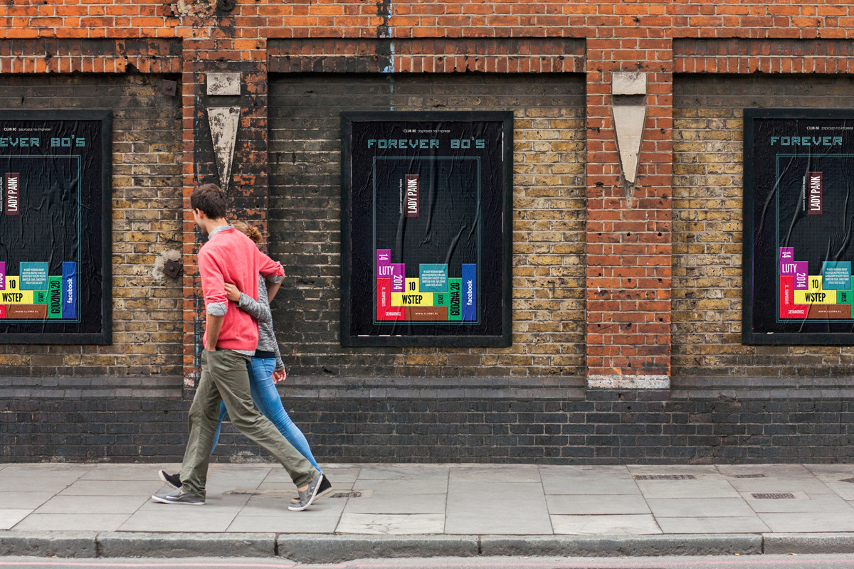 Para spaceruje chodnikiem obok ceglanej ściany z trzema plakatami wydarzenia muzycznego 'Forever 80's' z datą lutową i informacją o Lady Pank.