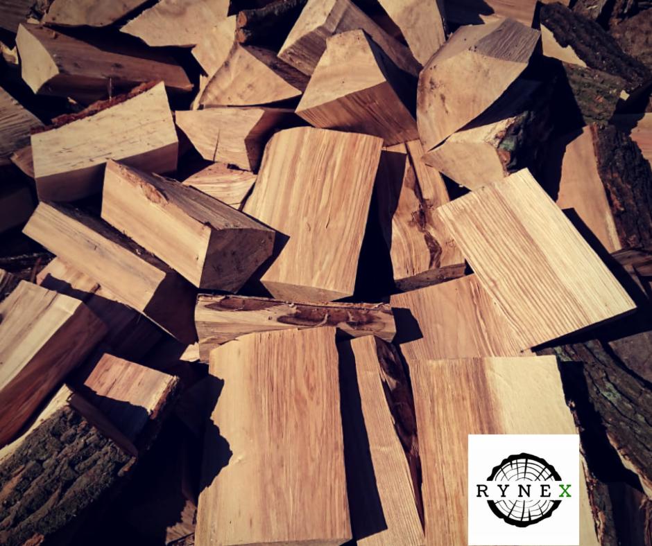 Stos pociętego drewna z widoczną korą i logo RYNEK w prawym dolnym rogu.