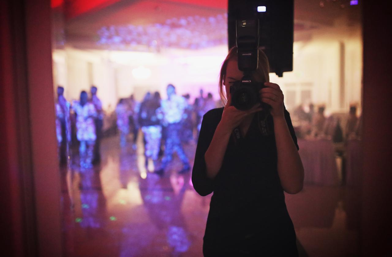 Kobieta fotografująca Canonem z lampą błyskową na tle rozświetlonego parkietu i bawiących się ludzi podczas wydarzenia.
