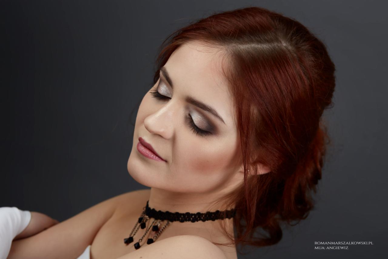Portret kobiety z zamkniętymi oczami, prezentującej srebrzysto-szary makijaż oczu i delikatny róż na ustach, z upiętymi rudymi włosami i czarnym koronkowym chokerem na szyi na ciemnoszarym tle.