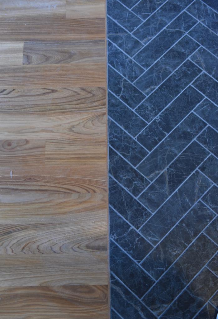 Połączenie paneli drewnianych i płytek imitujących marmur ułożonych we wzór jodełki, widoczne z góry.