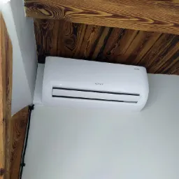 Biała jednostka klimatyzacji Rotenso zamontowana na ścianie w pomieszczeniu z drewnianym stropem i belkami.