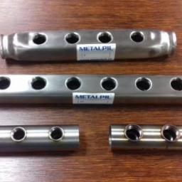 Metalpil Sp z o.o. - Metalowe rury o różnych długościach z wywierconymi otworami, ułożone na drewnianym blacie, z naklejonymi etykietami producenta.