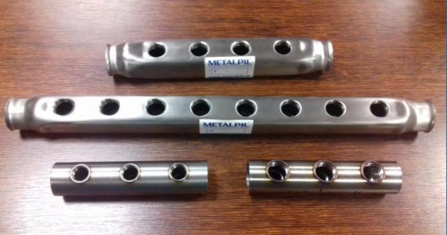 Metalowe rury o różnych długościach z wywierconymi otworami, ułożone na drewnianym blacie, z naklejonymi etykietami producenta.