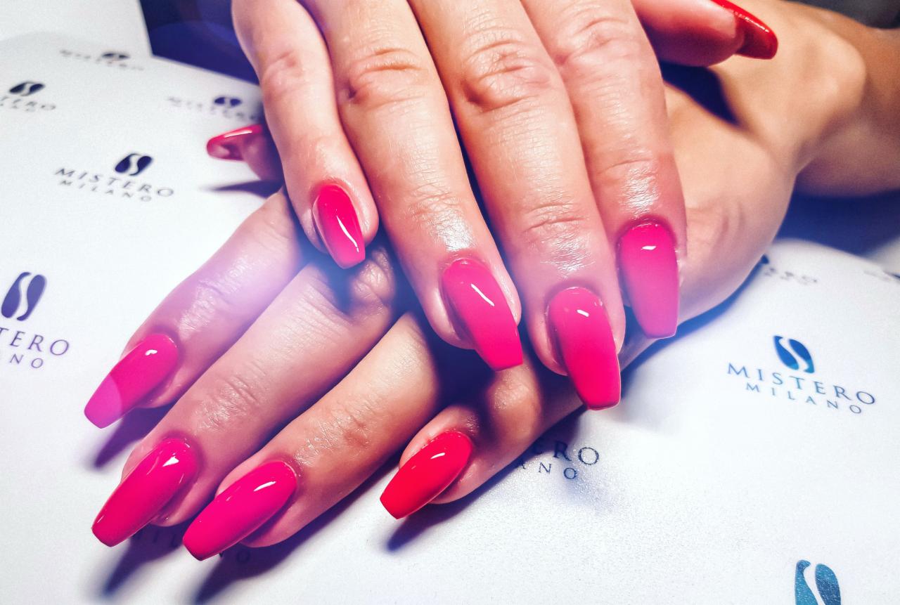 Dłonie z pomalowanymi na intensywny róż paznokciami w kształcie trumienki, na tle z logo Mistero Milano.