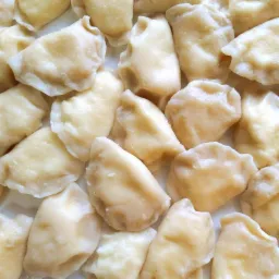 Świeżo ugotowane pierogi z bliska, widoczne lekkie zmarszczenia na cieście i delikatny połysk.