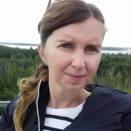 Portret kobiety na tle rozległego lasu i jeziora, widocznych z platformy widokowej.